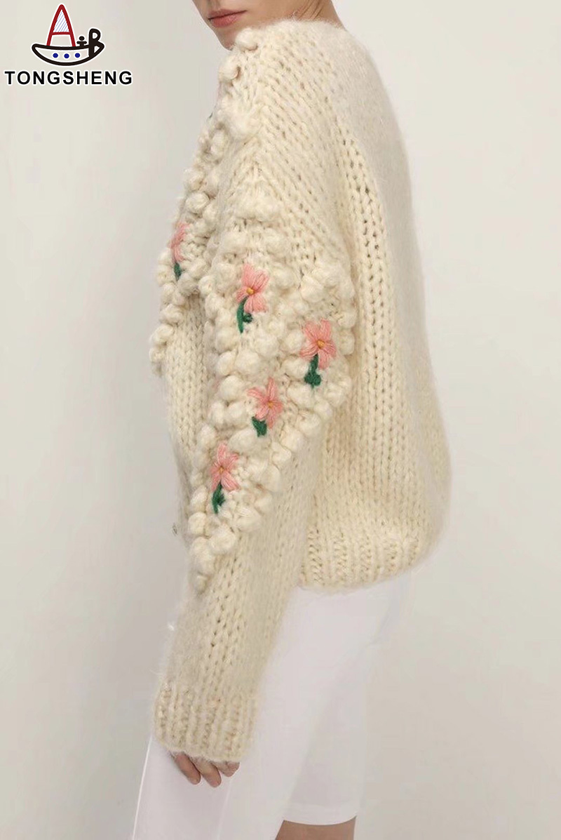 Ladies cardigan with a series of small balls and three pink flowers on the sleeves